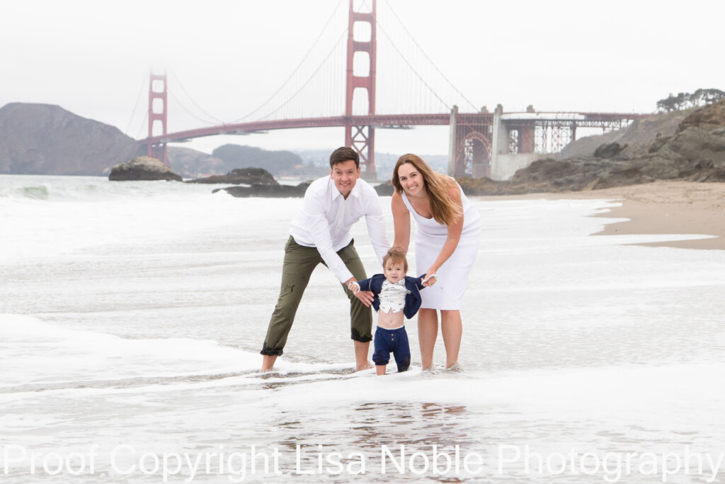 Family at photography session standing on Beach with Golden Gate Bridge in Background